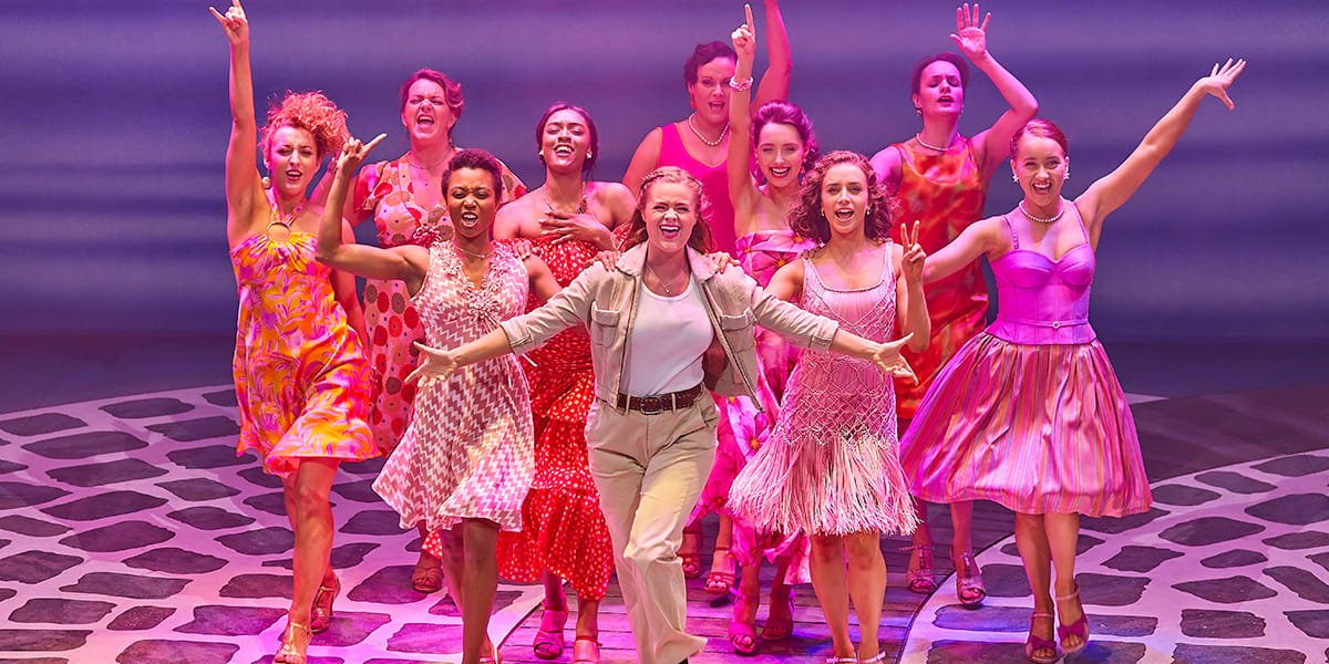 LtoR Melissa Nettleford as Ali, Lucy May Barker as Sophie, Sophie Matthew as Lisa with the cast of MAMMA MIA_ Credit Brinkhoff & Mögenburg