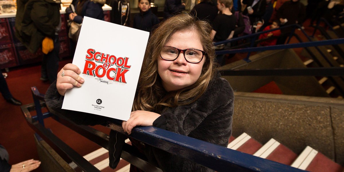 A girl enthusiastically presents a sign that says 'School Rocks' at a relaxed performance, embodying her love for school.
