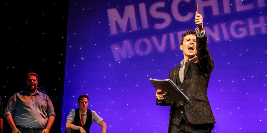 Man stands with a notepad holding a pen into the air.