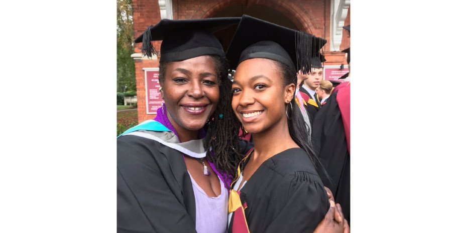 Two women stand facing each other wearing graduation robes