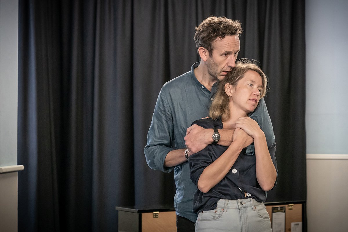 Chris O'Dowd stands behind Anna Maxwell Martin. He holds her and she in turn holds his arm. He is kissing her on the head.