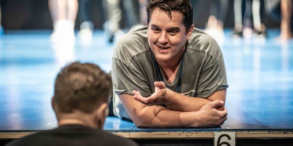 Craig Gallivan (Olaf) lies on stage leaning off edge talking to someone