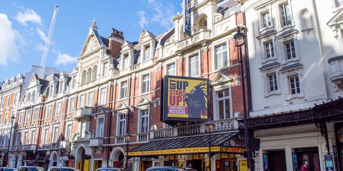 Nica Burns smiling, wearing a black blazer, with a blurred background of an event setting.