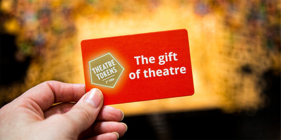 A collection of theatre tokens displayed on a wooden surface, featuring various colours and designs.