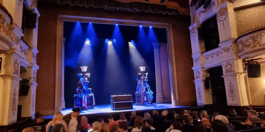 The stage. A bare stage with two coat hangers with clothes on to the side and a chest in the middle