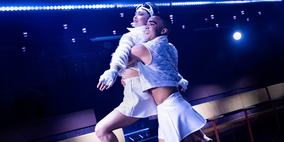 Two dancers dressed in white hold each other as one leaps.