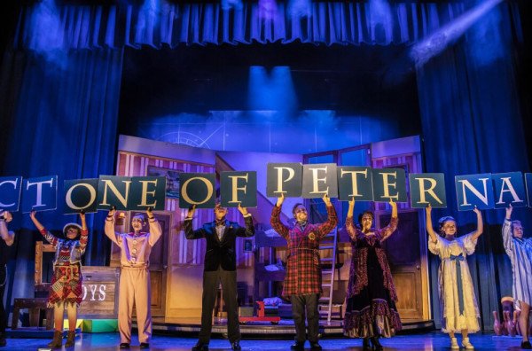 The cast of Peter Pan Goes Wrong hold up signs on a stage