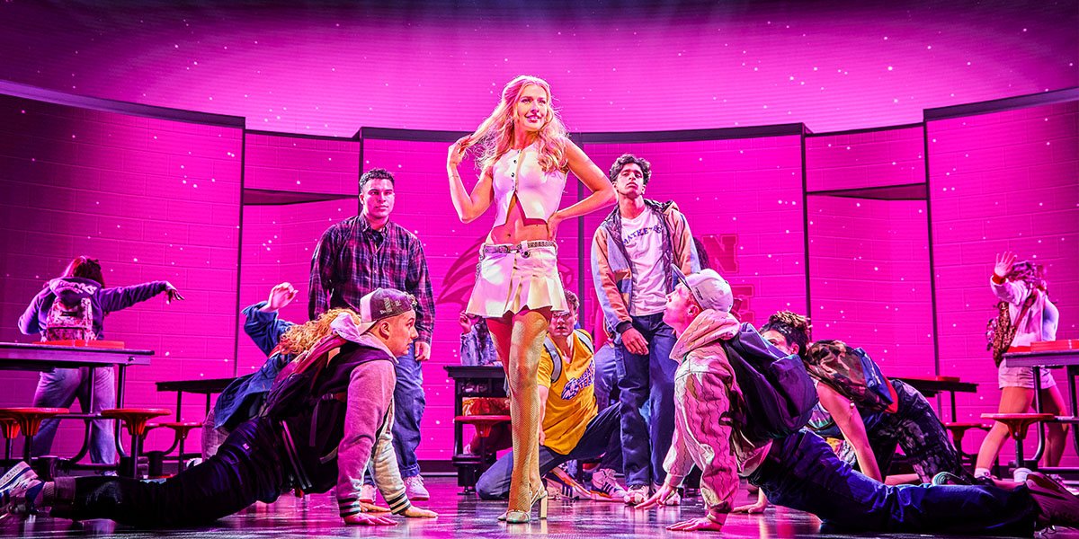 Georgina Castle (Regina) posing in the middle of the school cafeteria, surrounded by the Mean Girls ensemble including four performers laying down either side of her.