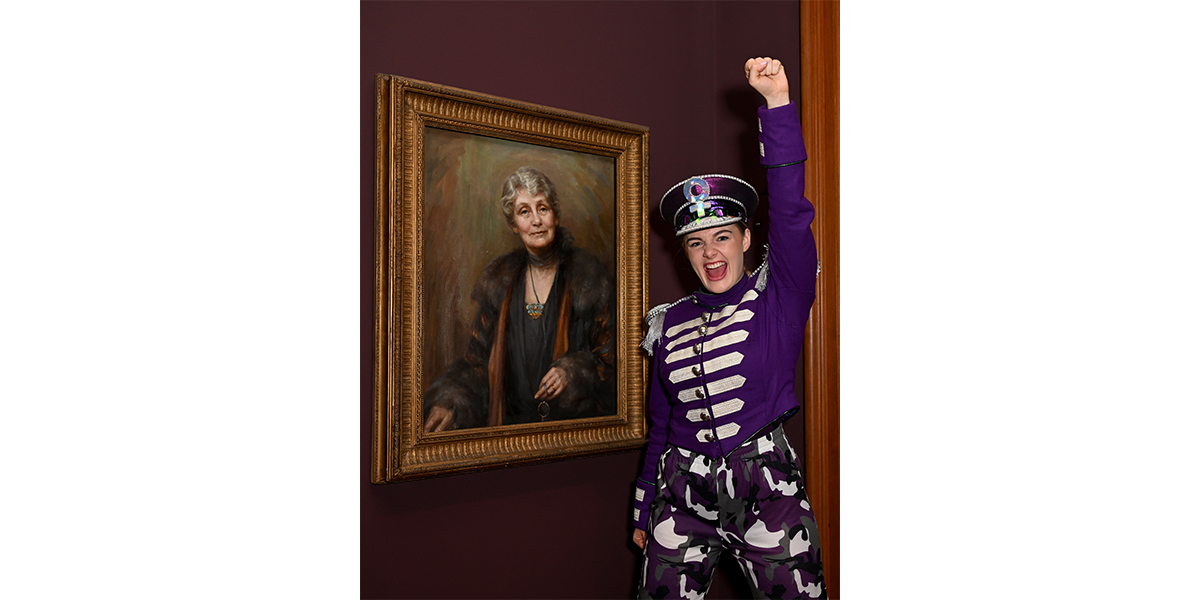 A woman stands in a purple military outfit in front of a portrait