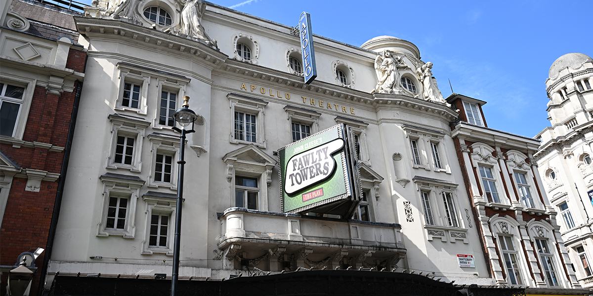 A stage scene from Fawlty Towers at the Apollo Theatre, featuring actors in period costumes and vibrant set design.